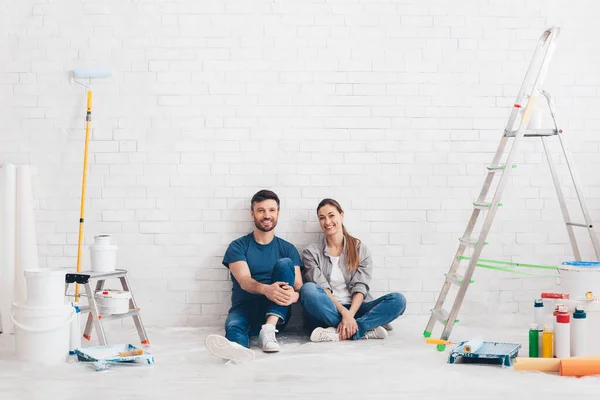 Νεαρό ζευγάρι που αγαπούν κάθεται σε εσωτερικούς χώρους σε νέο διαμέρισμα με εργαλεία ζωγραφικής — Φωτογραφία Αρχείου