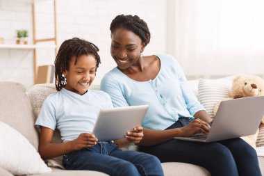 Afro anne ve kızı kanepede ödev yapıyor.