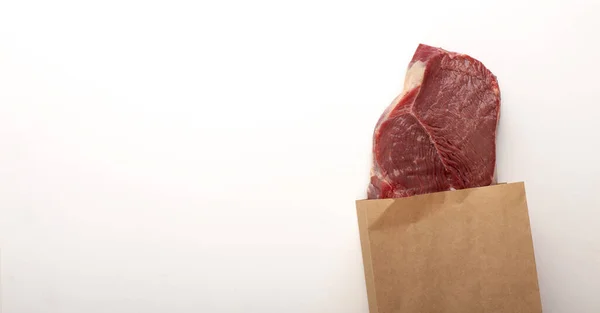 Carne cruda in sacchetto di carta su sfondo grigio — Foto Stock