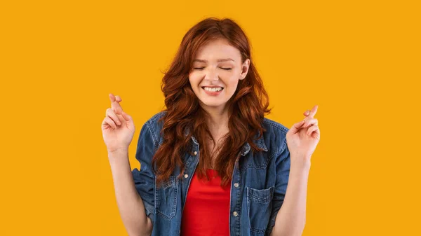 Chica manteniendo los dedos cruzados haciendo deseo posando sobre fondo amarillo —  Fotos de Stock