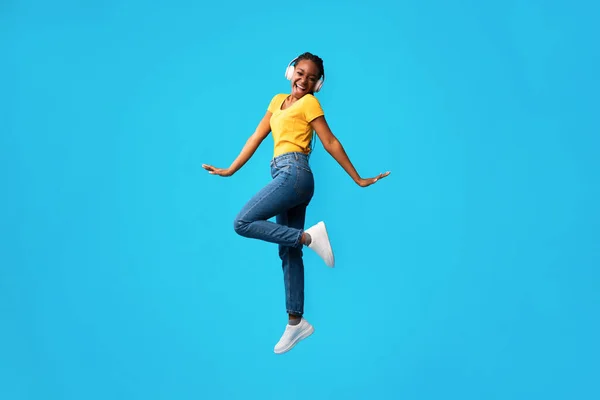 Menina em fones de ouvido saltando e cantando música em fundo azul — Fotografia de Stock