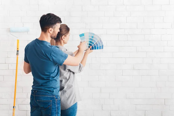 Casal jovem escolhendo a cor azul na paleta para pintar paredes — Fotografia de Stock