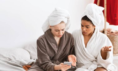 Shocked girlfriends in bathrobes looking at mobile phone