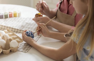 Little child with grandma painting eggs for Easter, closeup view