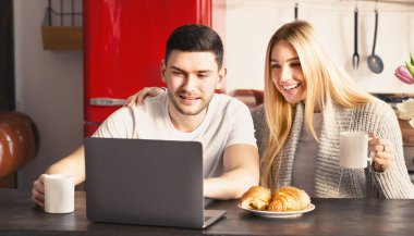Family of two having breakfast while using laptop in kitchen, panorama