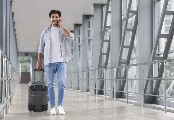 Man traveller walking with luggage in airport and talking on cellphone — Stockfoto