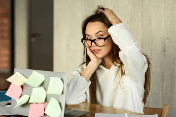 Surprised millennial girl scratches head at work — Zdjęcie stockowe