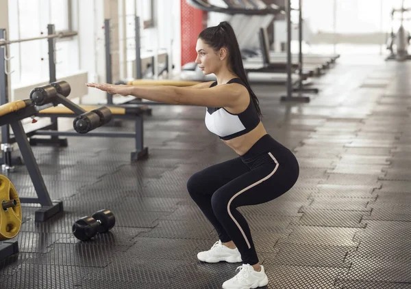 Charming girl in sportswear doing squats in gym — Stok fotoğraf