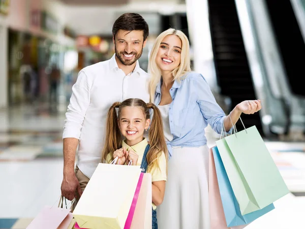 Família de três posando com sacos de compras no centro comercial — Fotografia de Stock