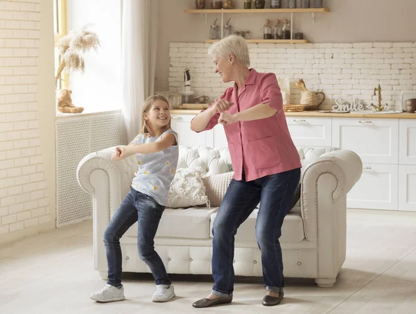 Cheerful older lady with her granddaughter dancing at home — Stock Photo, Image