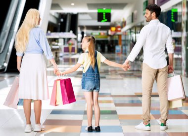 Parents And Daughter Standing Holding Hands In Mall, Back View
