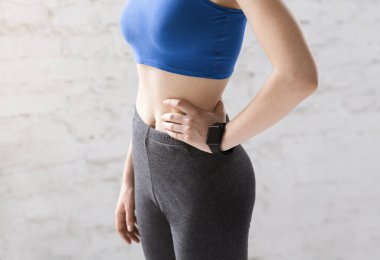 Unrecognizable slim young gymnast in sportswear against white wall, closeup of flat belly