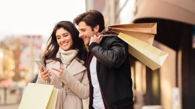 Young couple using phone after shopping in mall