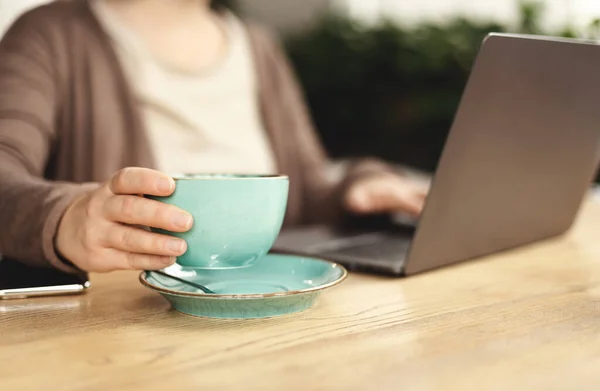 Размытая женщина работает на ноутбуке и пьет кофе — стоковое фото