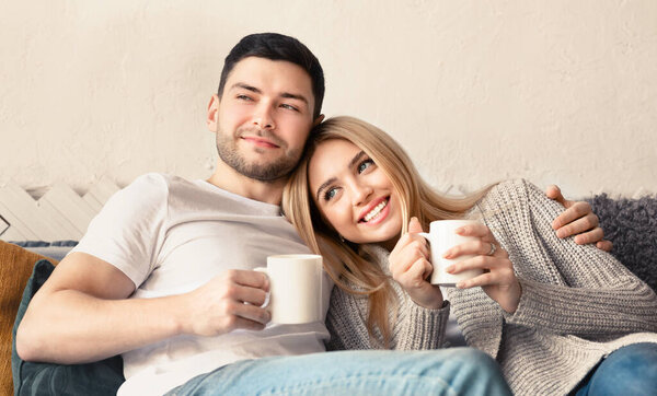 Handsome guy and his girlfriend with hot drinks spending time together at home, panorama