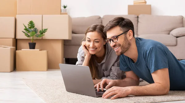 Happy couple searching online with a laptop over a cardboard box — Stock Fotó