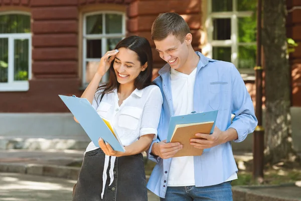 Alegre pareja de amigos de la universidad riendo al aire libre mientras revisa el horario de clases —  Fotos de Stock