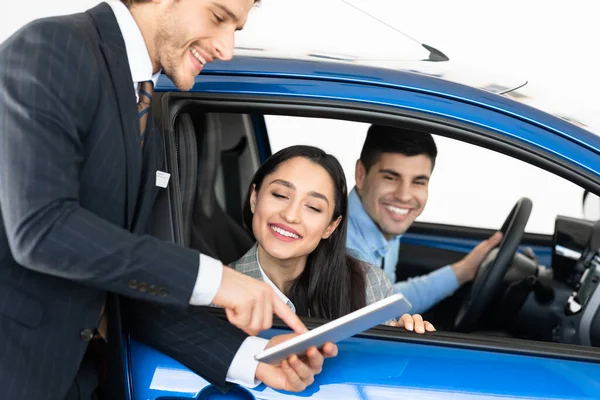 Casal feliz comprando carro conversando com revendedor sentado em automóvel — Fotografia de Stock