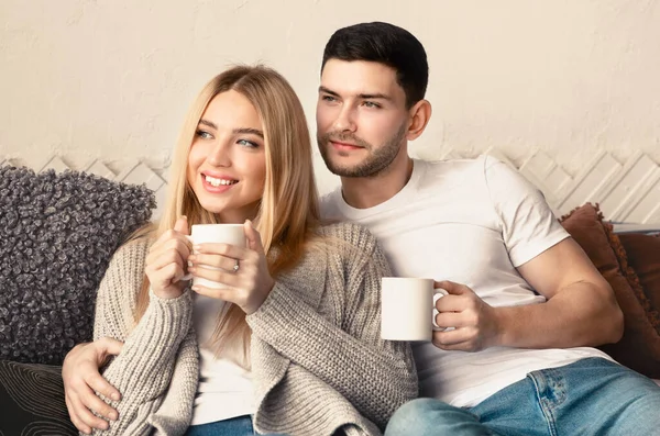 Recém-casados com chá quente abraçando no sofá dentro de casa — Fotografia de Stock