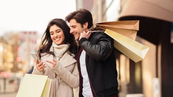 Young couple using phone after shopping in mall — 图库照片