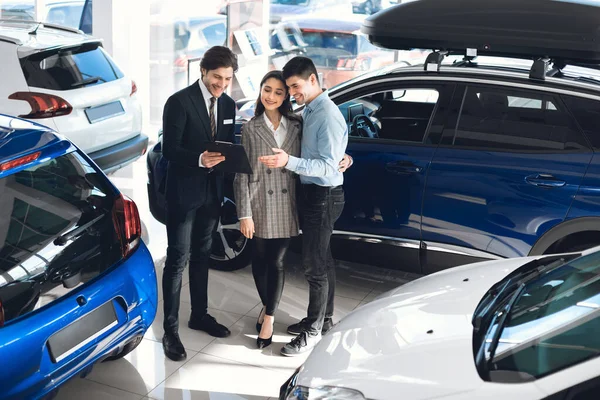 Vendedor ofreciendo pareja un coche de pie en la oficina de alquiler — Foto de Stock