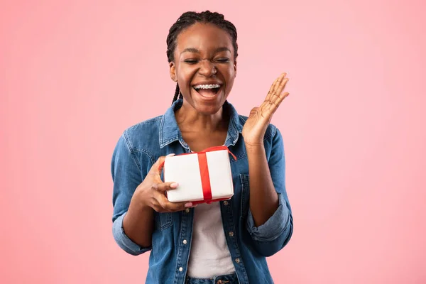 Щаслива чорна дівчина тримає подарункову коробку сміючись над рожевим тлом — стокове фото
