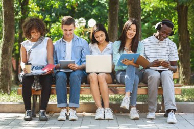 Group of students with laptop and tablet computer studying together outdoors