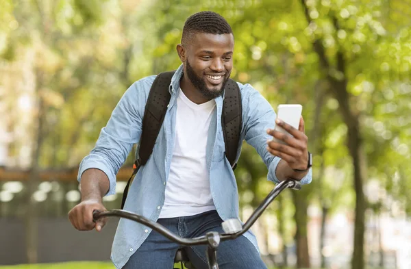 Alegre afro-americano cara tendo vídeo chamada enquanto dirigindo bicicleta ao ar livre — Fotografia de Stock