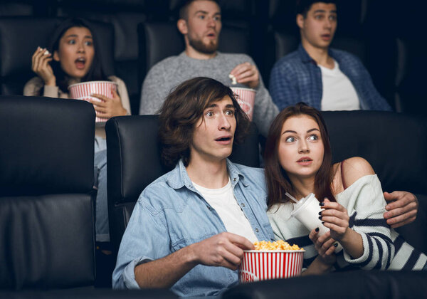Frightened couple watching thriller on night out in cinema