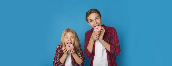 Preteen broers en zussen eten donuts, poseren over blauwe achtergrond — Stockfoto