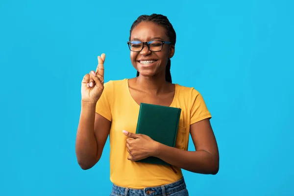Estudiante chica mantener los dedos cruzados sosteniendo libros sobre fondo azul — Foto de Stock