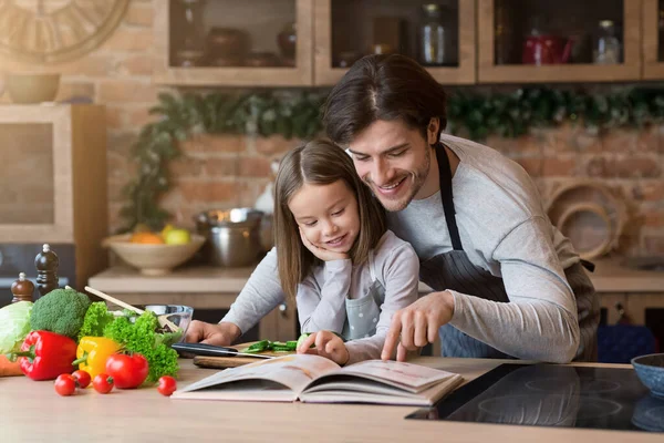 Happy dad and little daughter checking recipe in cookbook together — Stockfoto