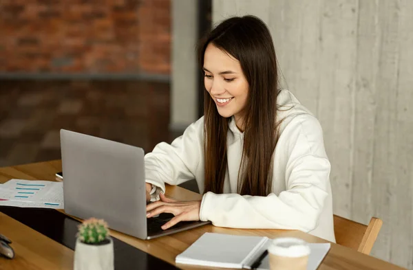 Sorrisos menina com laptop funciona à mesa — Fotografia de Stock