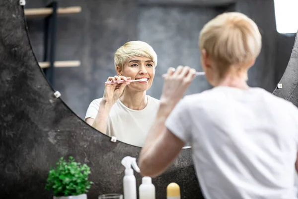 Счастливая женщина чистит зубы утром, стоя в ванной — стоковое фото