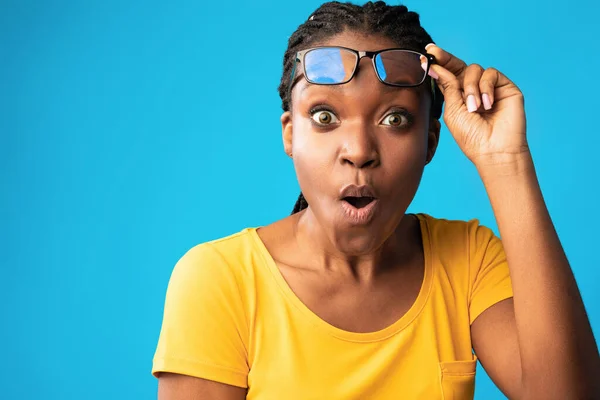 Shocked African Woman Looking At Camera Rising Eyeglasses, Blue Background — Stock Photo, Image
