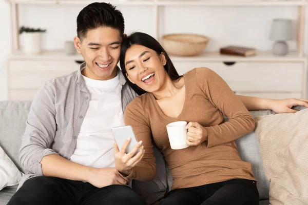 Asian couple resting at home, using phone — Stock fotografie