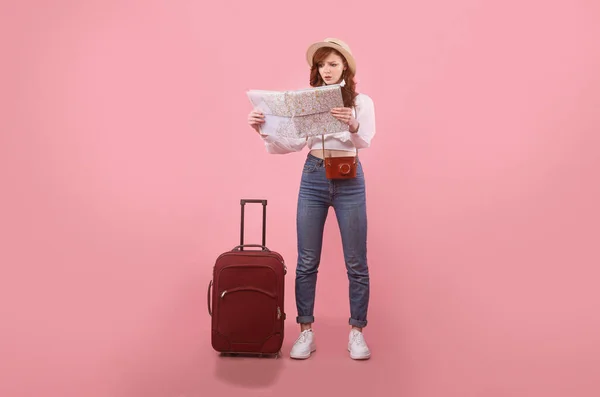 Μπερδεμένη κοπέλα κοιτάζοντας το χάρτη στέκεται με τη βαλίτσα, Studio Shot — Φωτογραφία Αρχείου