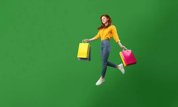 Glad flicka hoppa med shoppingväskor över grön studio bakgrund — Stockfoto