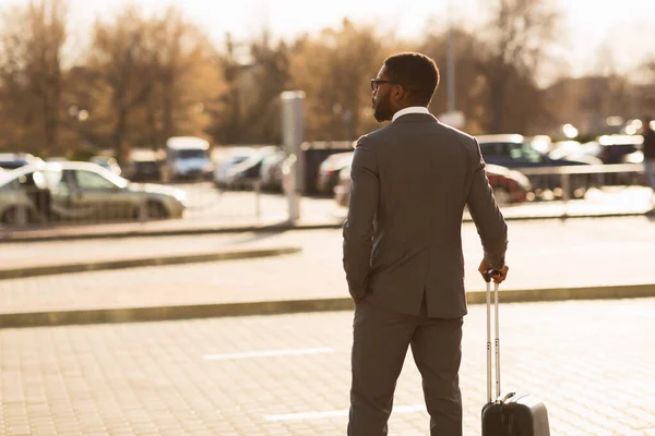 Предприниматель, стоящий с чемоданом на парковке железнодорожного вокзала, вид сзади — стоковое фото