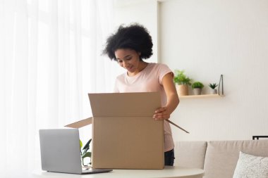 Surprised american young woman with laptop opens box