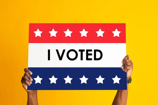 African American US resident holding banner in national colors with inscription I VOTED on orange background — стокове фото