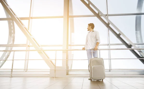 Feliz hombre de pie con la maleta cerca de la ventana en la terminal del aeropuerto — Foto de Stock