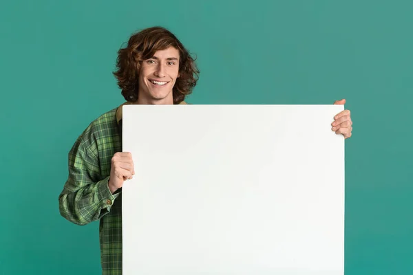 Happy millennial guy holding blank banner on turquoise background, space for design — Stock Fotó
