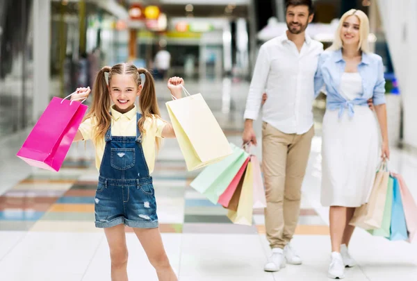 Menina levando sacos comprando roupas com pais no shopping — Fotografia de Stock