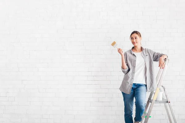 Young woman with paint brush in new flat over white bricks wall — Φωτογραφία Αρχείου