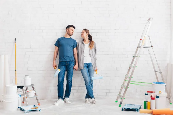 Happy young couple holding paint rollers and smiling each other — Stock Photo, Image