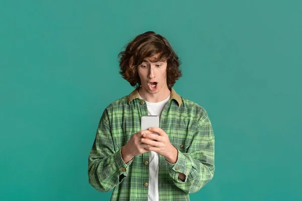 Lottery winner. Cool teenager looking at smartphone and shouting WOW on turquoise background — Stockfoto