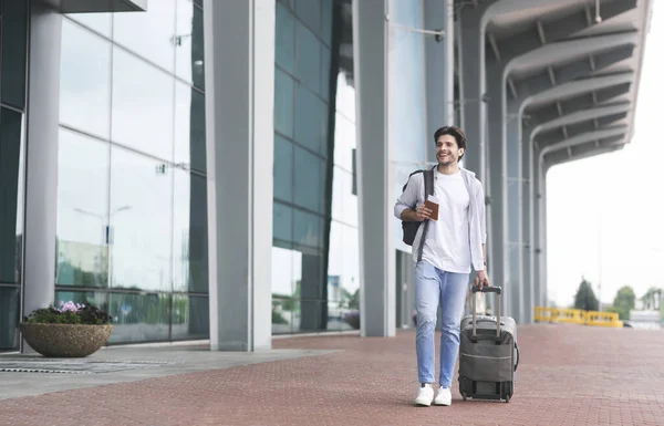 Jovem feliz andando com mala e mochila perto do terminal do aeroporto — Fotografia de Stock