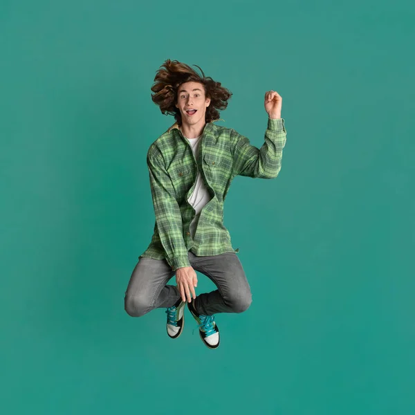 Happiness and freedom. Cheerful young guy in casual clothes jumping on turquoise background — Stok fotoğraf