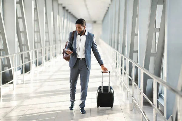 Empreendedor usando Smartphone andando no aeroporto com mala interior — Fotografia de Stock